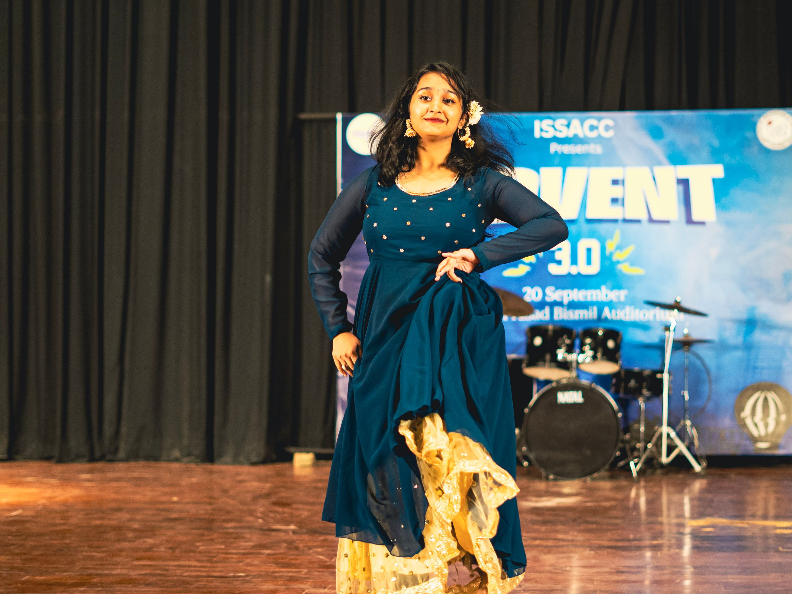 A dancer in a blue lehenga posing on a lit auditorium stage