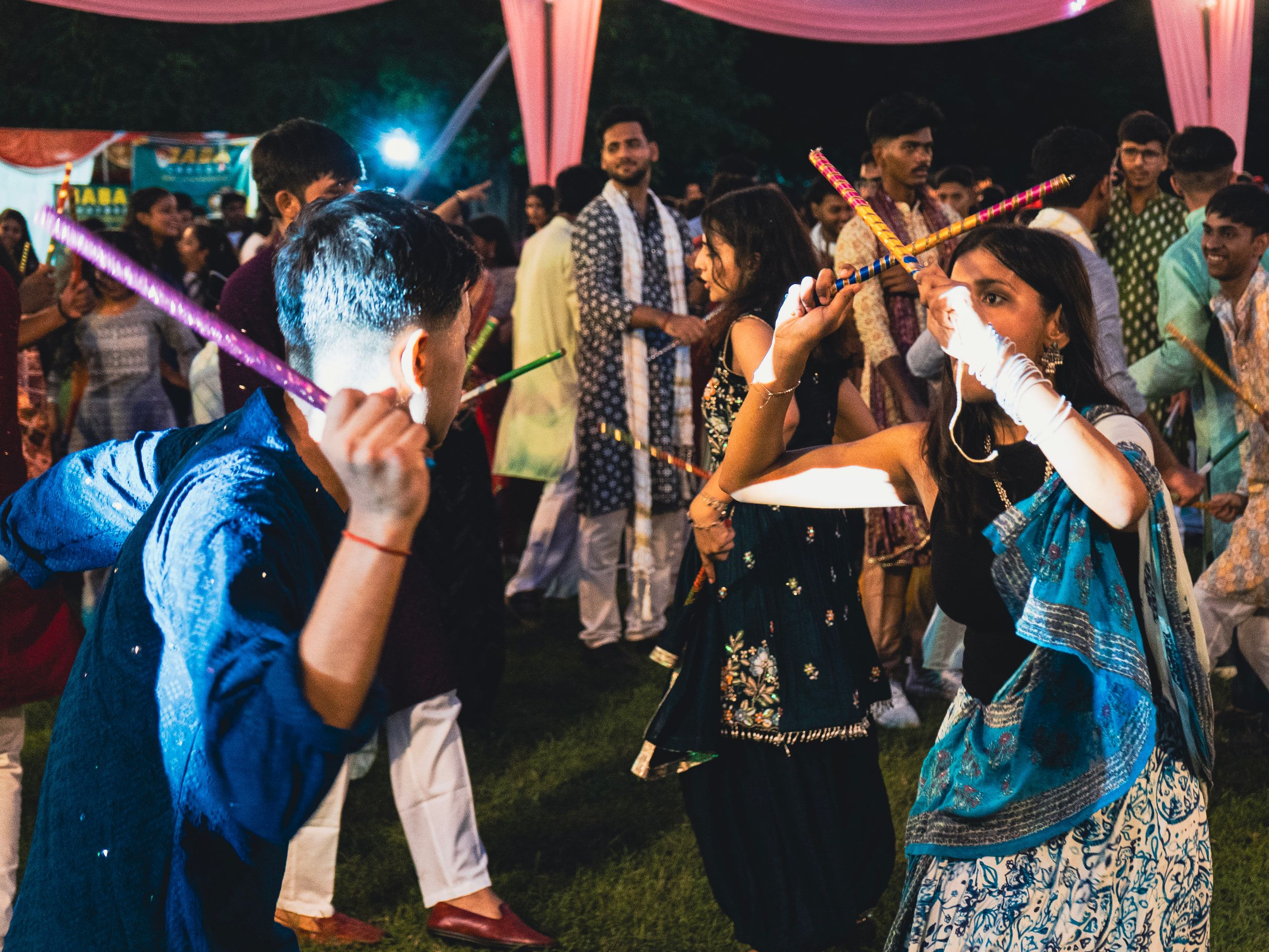 A crowd mid-dance with glowing dandiya sticks at a garba night