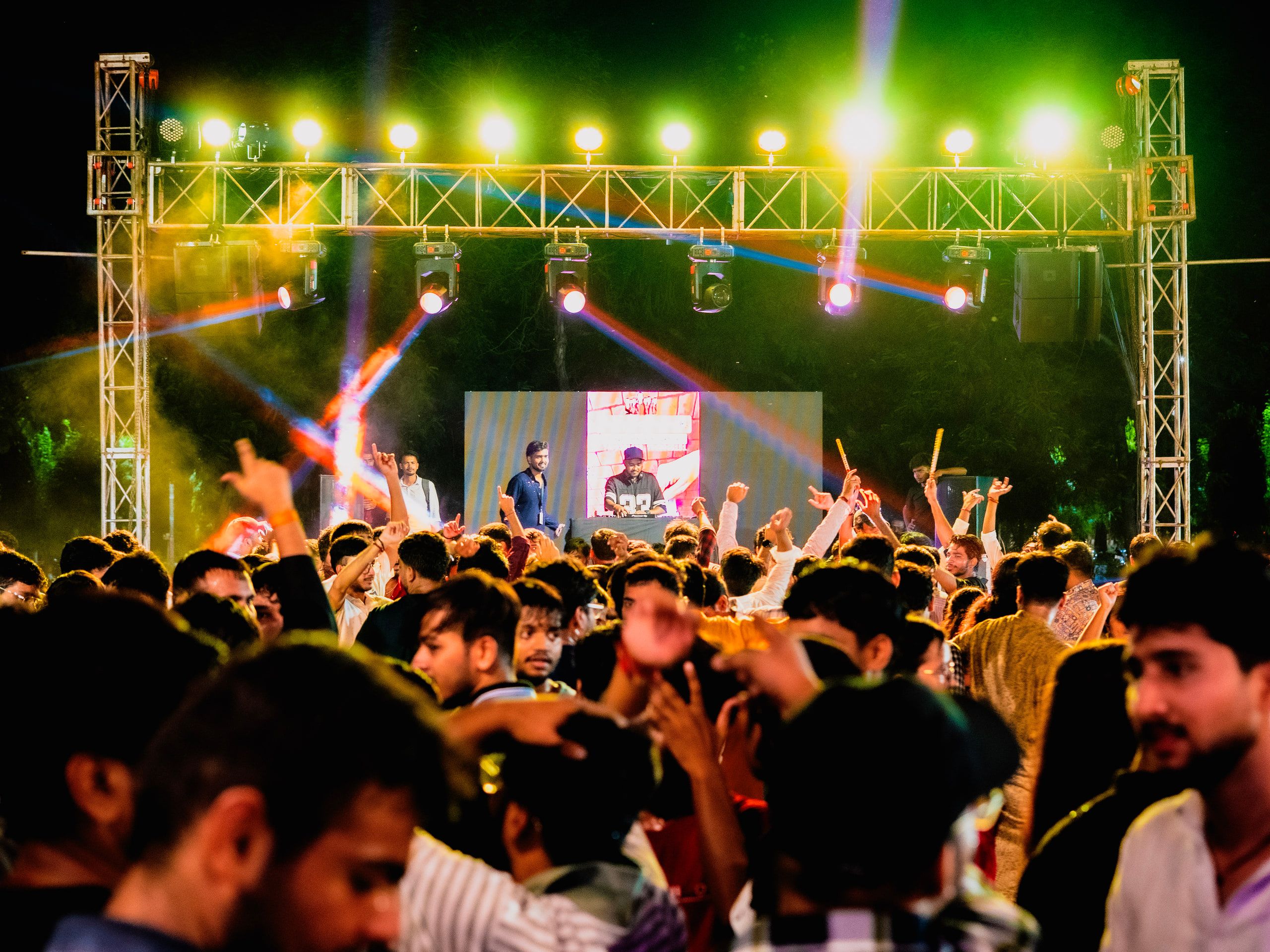 A crowd with hands up in front of a brightly lit festival stage at night