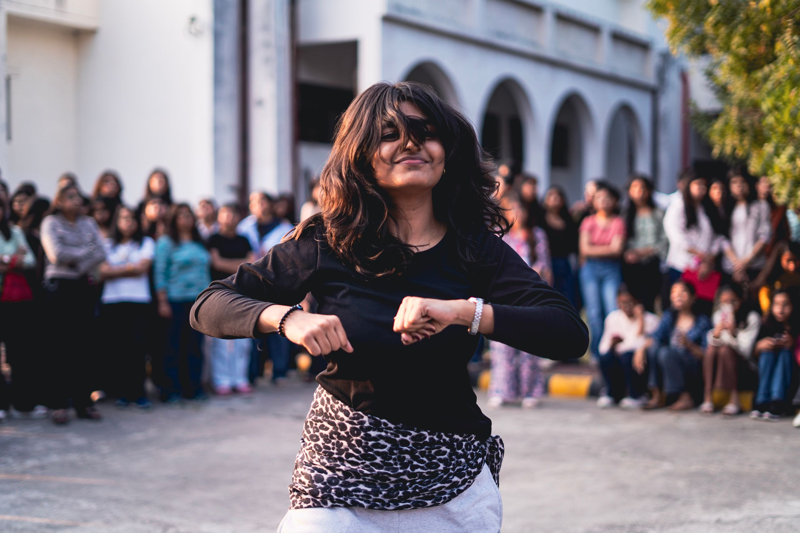 A woman dancing in a college courtyard surrounded by a crowd