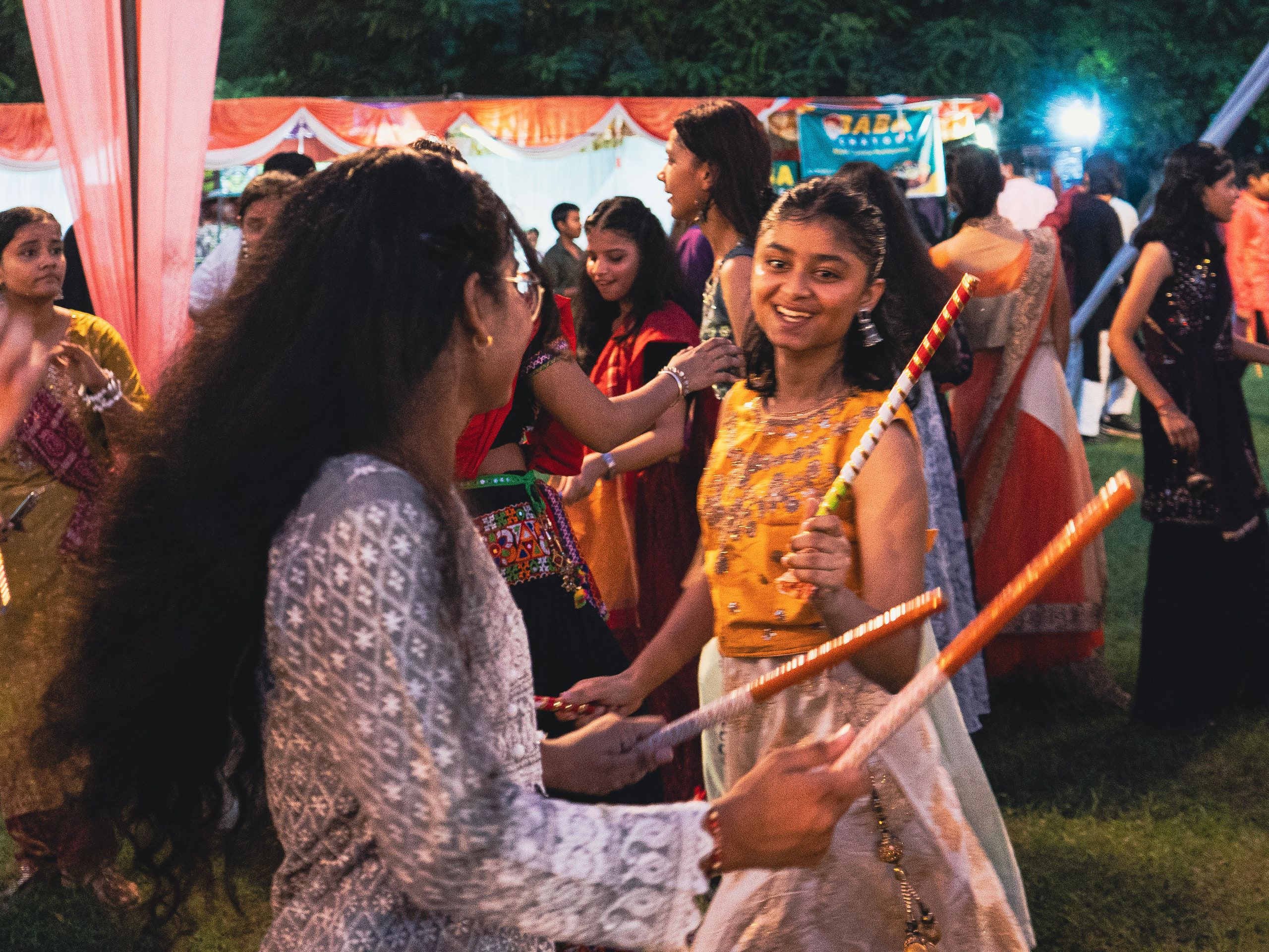 Friends dancing with dandiya sticks under a colourful canopy