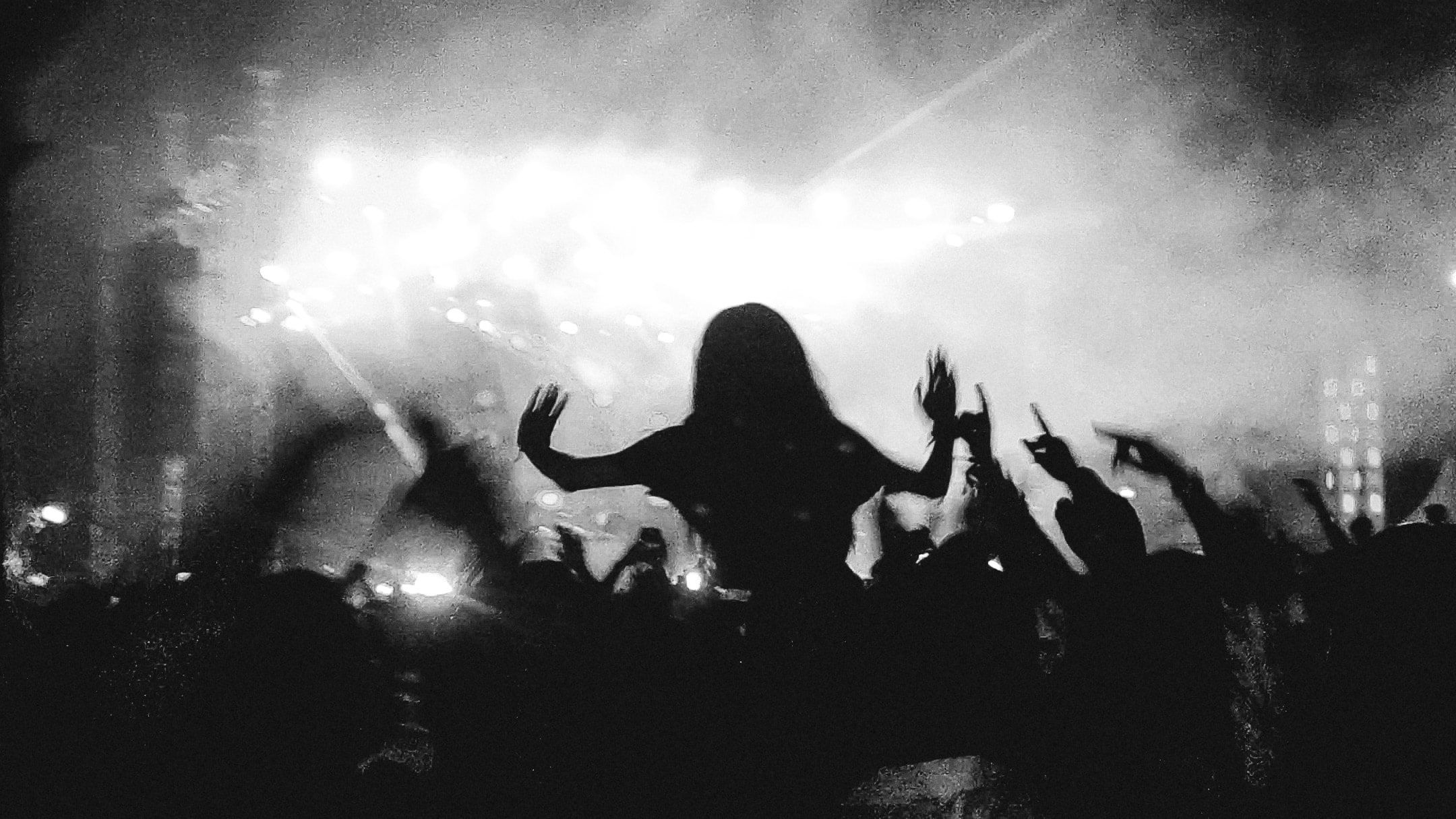 Black and white silhouette of a crowd with hands raised in stage smoke