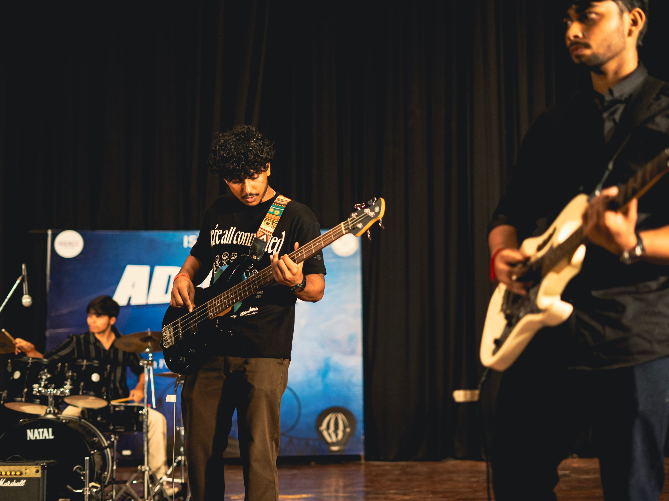 A band playing guitars and drums on an auditorium stage