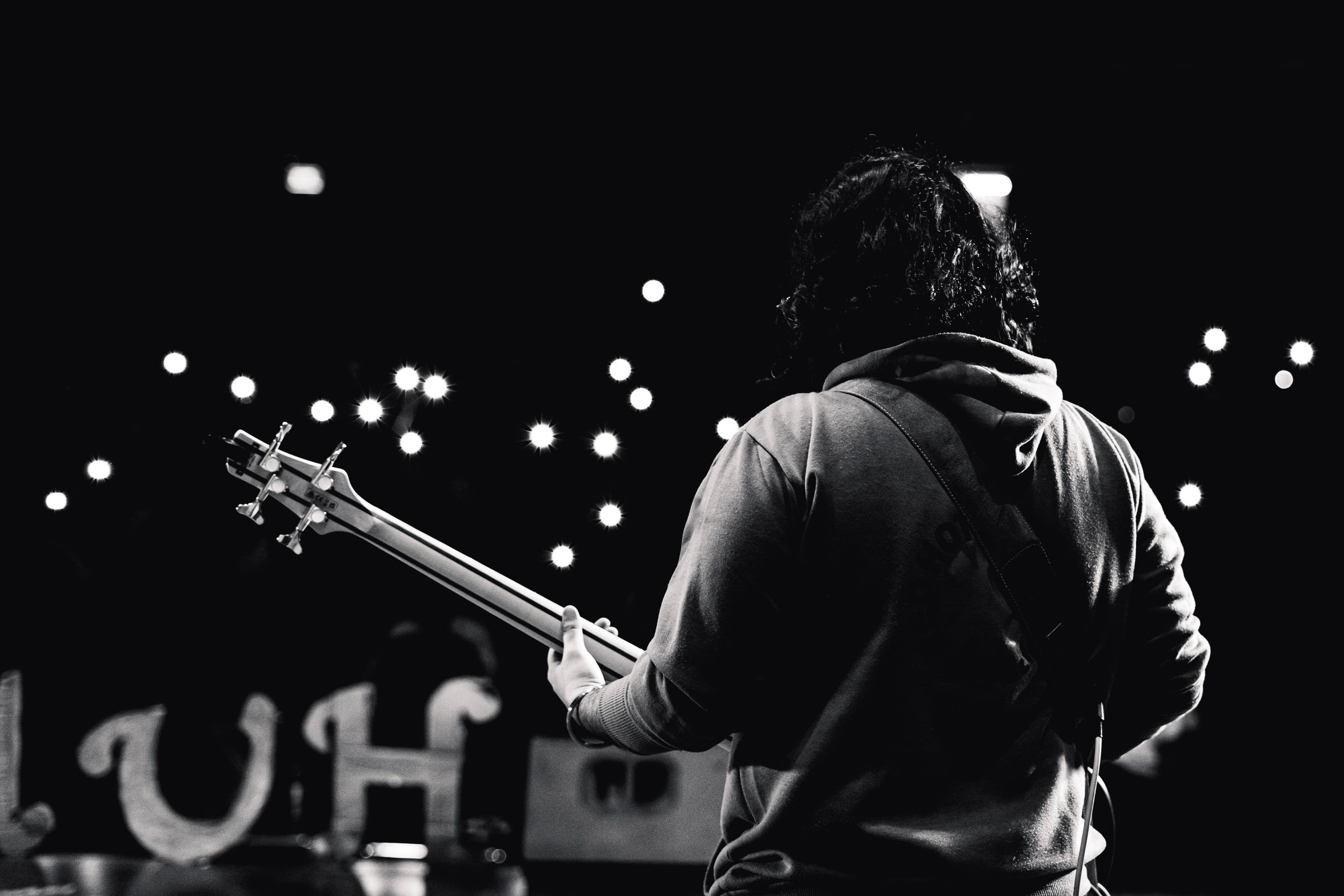 Black and white shot of a bassist facing a field of lights