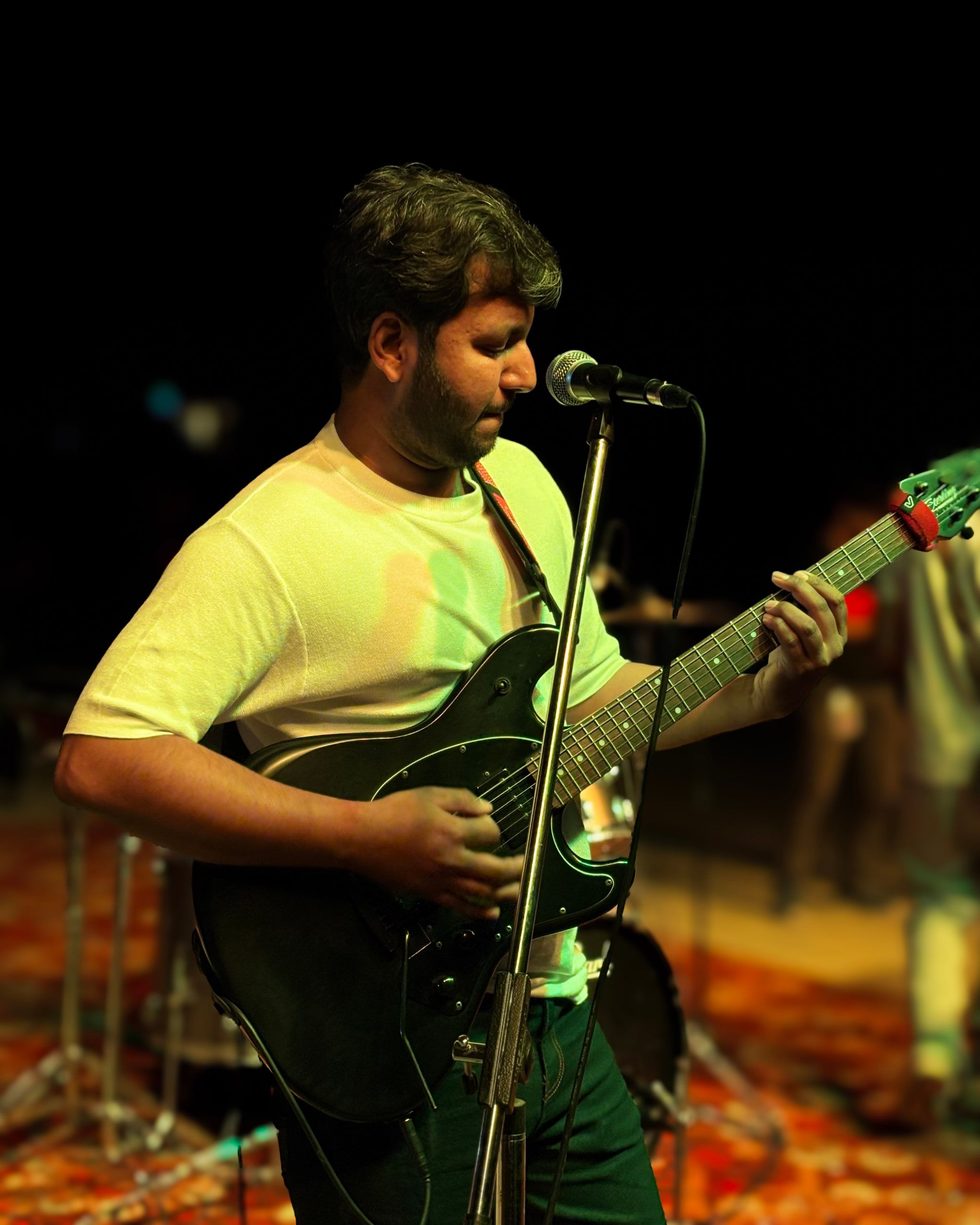 A guitarist in a yellow T-shirt singing on stage