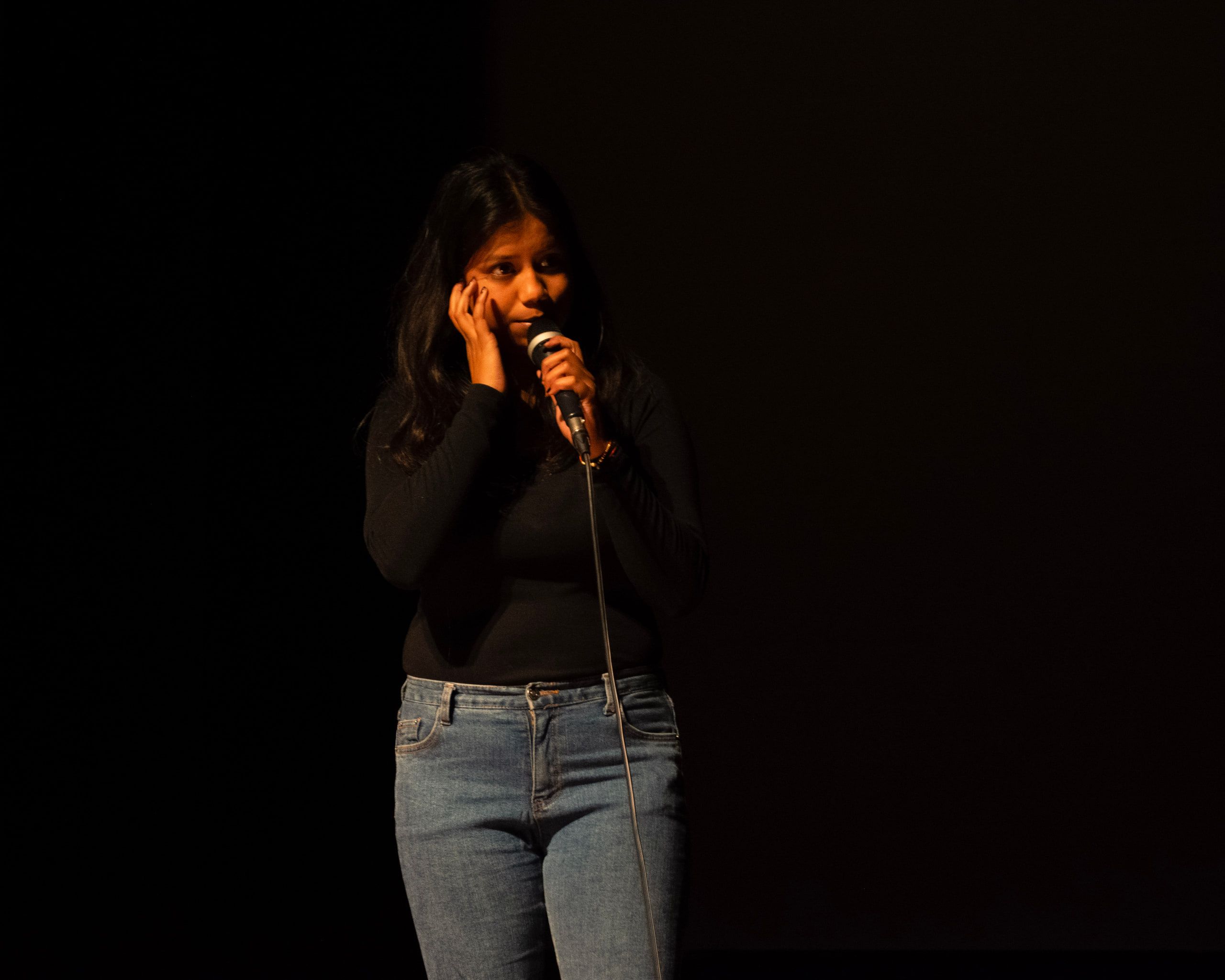 A singer with a microphone lit softly against a dark stage