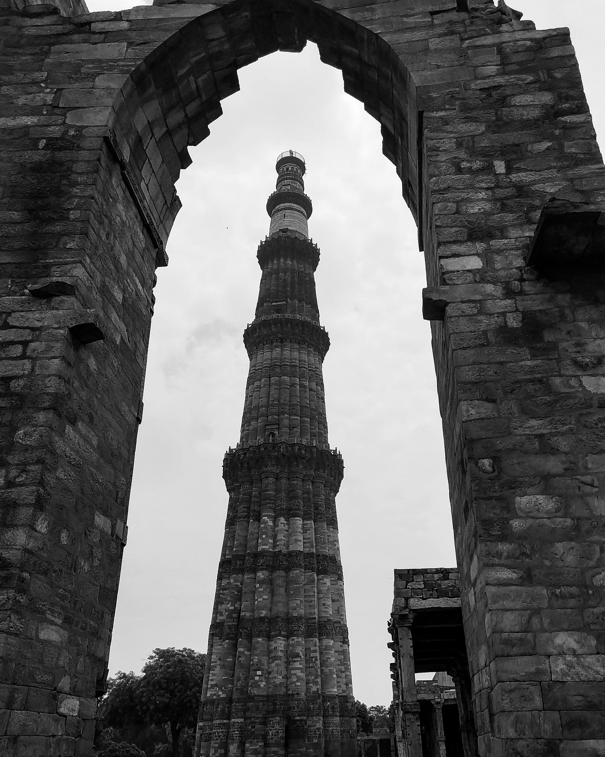 Black and white view of Qutub Minar framed by a ruined stone arch