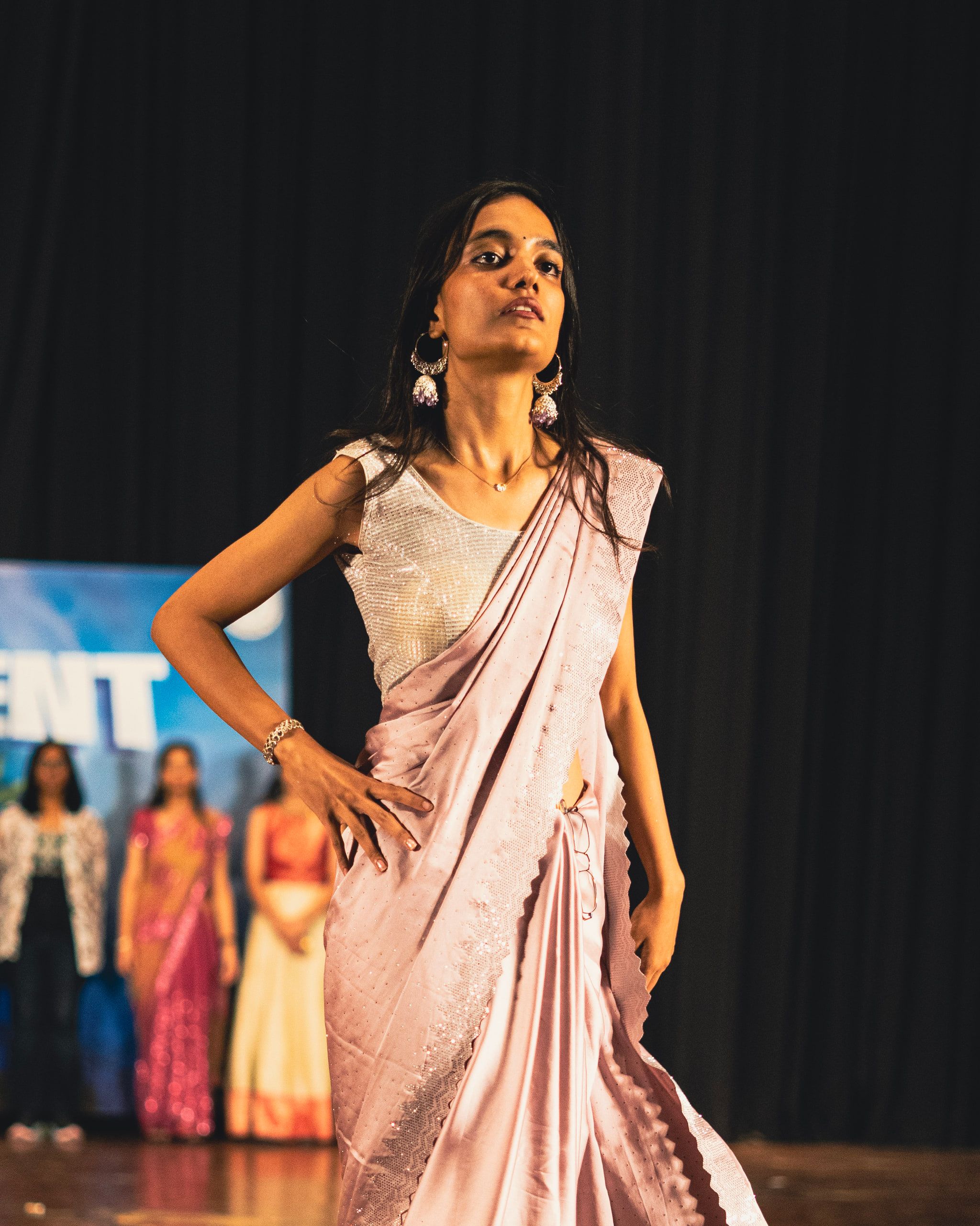 A woman in a pale pink saree posing on stage
