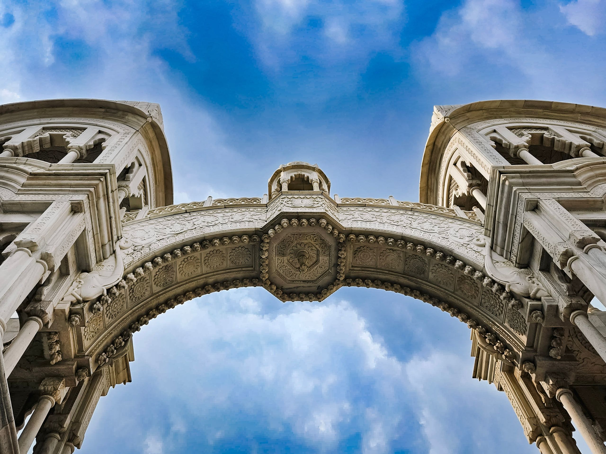 An ornate white stone arch framing blue sky and clouds