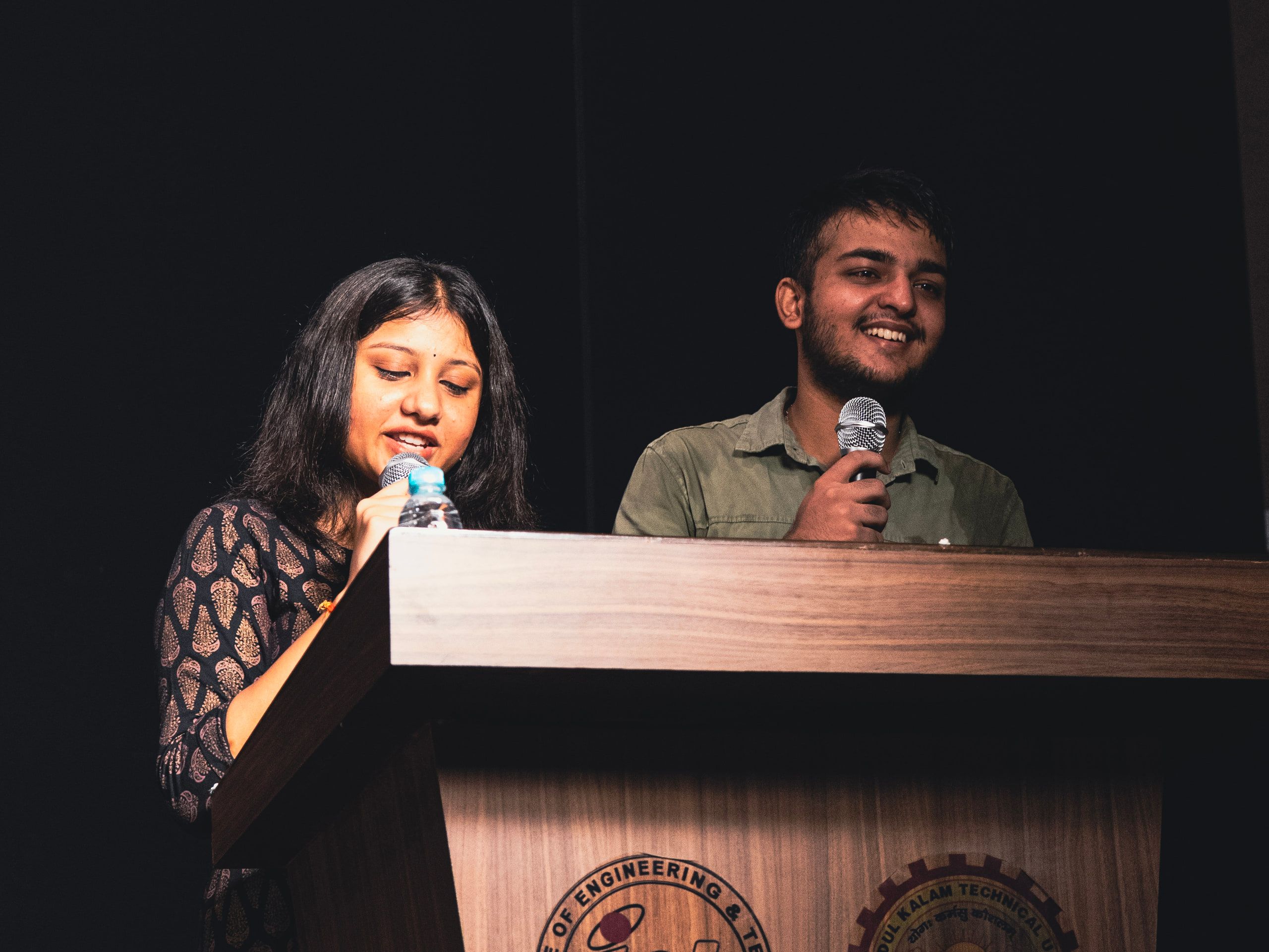 Two hosts speaking at a podium on stage