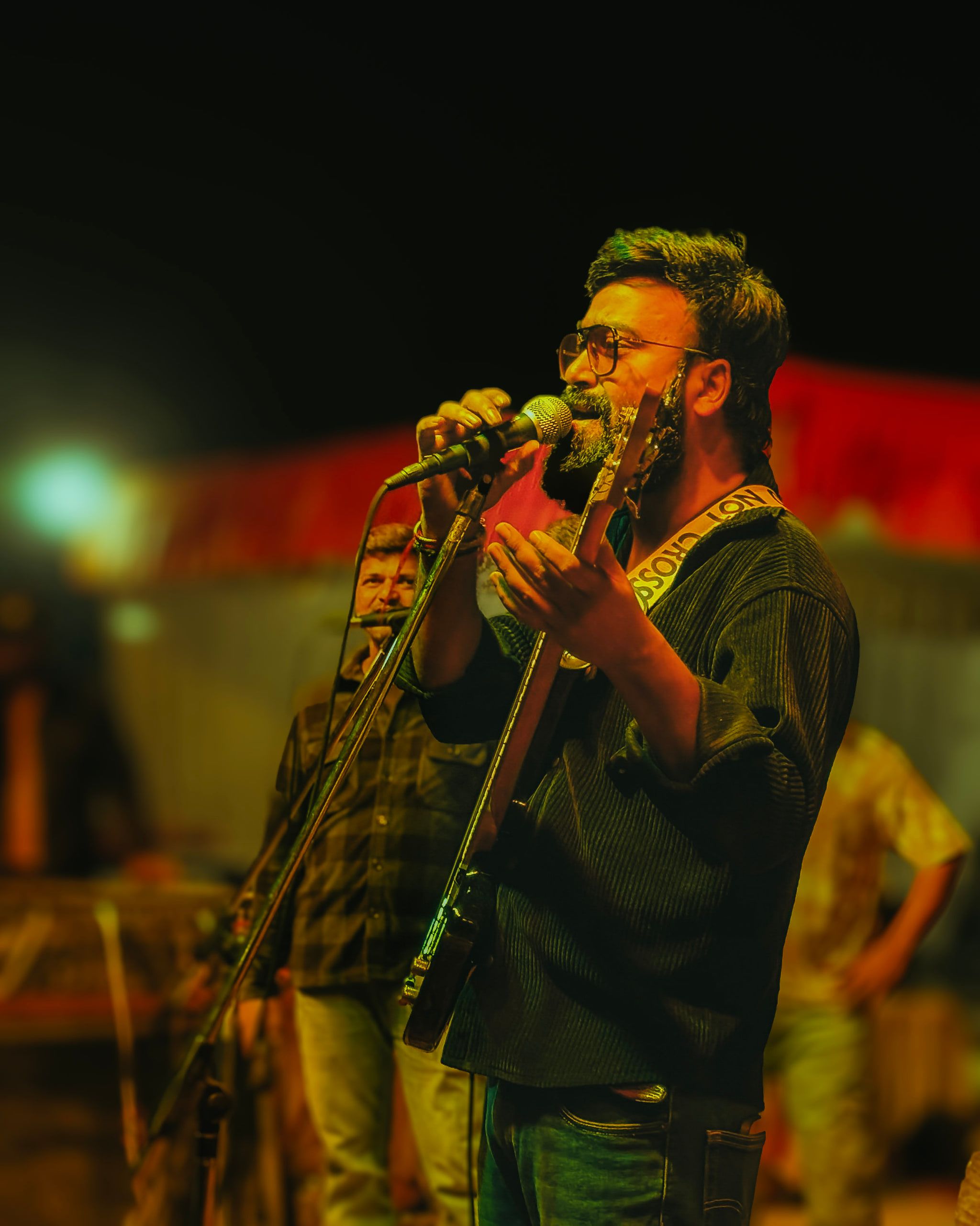 A guitarist singing under warm orange stage light